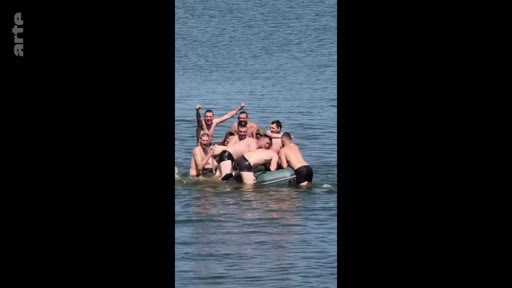 Un groupe de soldats russes en maillot de bain s'amuse et pose ensemble sur un petit canot pneumatique au milieu d'une étendue d'eau, illustrant des moments de camaraderie et d'humour au sein de l'armée.