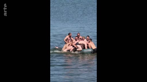 Un groupe de soldats en maillot de bain s'amuse ensemble sur un canot pneumatique gonflable en pleine mer, illustrant la camaraderie et l'humour au sein des forces armées.