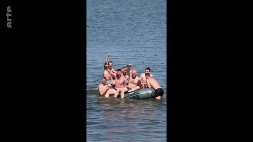 Un groupe d'hommes torse nu s'amuse et pose joyeusement sur un petit canot pneumatique gonflable en pleine mer, illustrant des moments de camaraderie et de détente.
