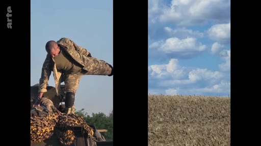 Un soldat ukrainien en tenue de camouflage monte sur un véhicule blindé recouvert d'un filet de camouflage dans un champ sous un ciel nuageux. Cette image illustre le quotidien des forces armées ukrainiennes sur le terrain lors du conflit en Ukraine.