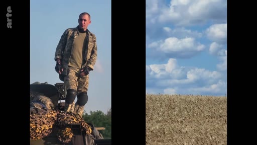 Un soldat ukrainien en tenue de camouflage est debout sur un véhicule blindé, probablement dans une zone de conflit en Ukraine. L'image montre le contraste entre la présence militaire et le paysage rural sous un ciel nuageux.