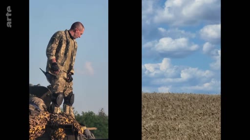 Un soldat ukrainien en uniforme de camouflage, équipé de genouillères et de gants, est debout sur un véhicule blindé dans un champ. Cette image illustre la présence militaire sur le terrain dans le contexte du conflit en Ukraine.
