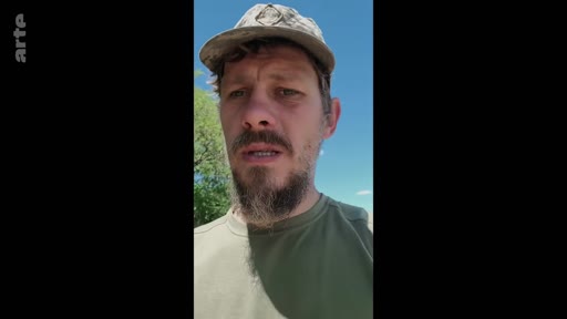 Un soldat en tenue militaire et casquette s'adresse à la caméra lors d'un témoignage en extérieur, probablement dans le cadre d'un reportage sur le front ou une zone de conflit.