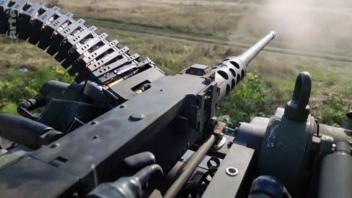 Vue à la première personne d'une mitrailleuse lourde Browning M2 en train de tirer, illustrant des opérations militaires sur le terrain. L'image montre le mécanisme de l'arme et la bande de munitions en mouvement lors d'un engagement armé.