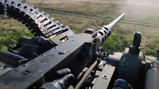 Vue à la première personne depuis une mitrailleuse lourde Browning M2 montée sur un véhicule militaire en opération. L'arme est chargée avec une bande de munitions, prête à l'emploi dans un contexte de combat ou d'entraînement militaire.