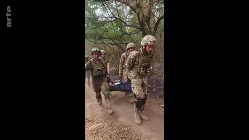 Des soldats ukrainiens en tenue de camouflage et équipés de casques transportent un camarade blessé sur une civière à travers une zone boisée. Cette scène illustre les opérations de secours et d'évacuation médicale sur le front ukrainien.