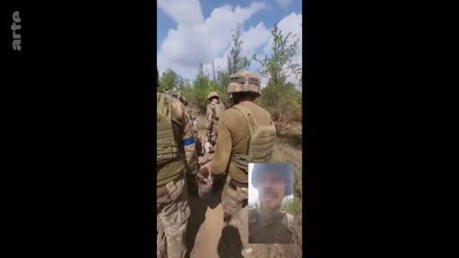 Des soldats ukrainiens en tenue de combat évacuent un camarade blessé sur une civière dans une zone boisée, tandis qu'un soldat filme la scène en mode selfie. Cette séquence illustre les conditions difficiles des opérations de secours médical sur le front ukrainien.
