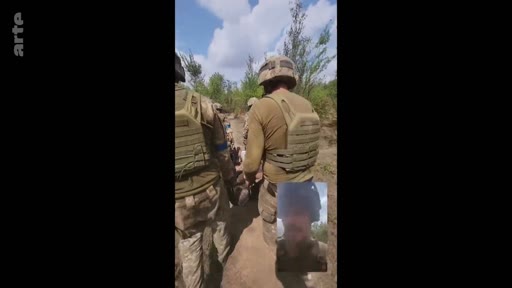 Des soldats ukrainiens en tenue de combat évacuent un camarade blessé sur une civière à travers une zone boisée, lors d'une opération sur le front. Une incrustation vidéo montre un soldat en gros plan, illustrant la réalité du terrain et les secours médicaux d'urgence en zone de conflit.
