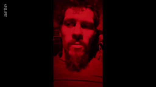 Un soldat barbu est filmé en gros plan dans une ambiance sombre avec un éclairage rouge intense, illustrant le quotidien des combattants sur le front.