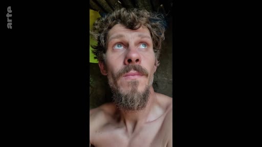 Un soldat barbu, filmé en gros plan, regarde vers le haut dans ce qui semble être une tranchée. Cette image illustre le quotidien difficile et l'attente des soldats sur le front.