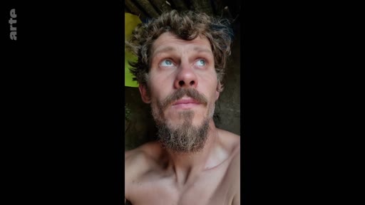 Un soldat barbu, torse nu, regarde vers le haut dans ce qui semble être une tranchée ou un abri de fortune. L'image illustre le quotidien difficile des militaires sur le terrain.