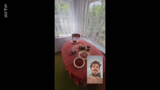 Un homme barbu apparaît en visioconférence sur un écran de téléphone, avec en arrière-plan une table dressée pour un repas dans une pièce lumineuse. Cette image illustre les liens familiaux maintenus à distance malgré le contexte de conflit.