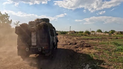 Un véhicule militaire chargé de matériel circule sur un chemin de terre dans une zone rurale, illustrant la progression des forces armées dans des villages libérés lors du conflit en Ukraine.