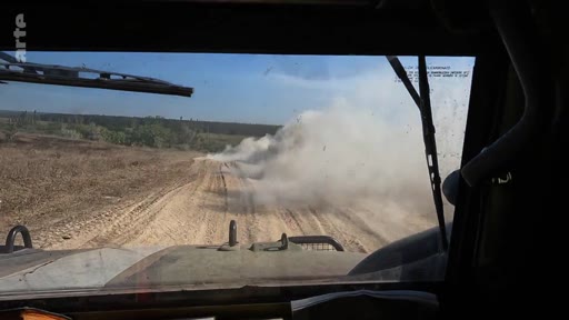 Vue subjective depuis le poste de pilotage d'un véhicule militaire en mouvement sur un terrain accidenté et poussiéreux, illustrant le quotidien des soldats en zone de conflit.