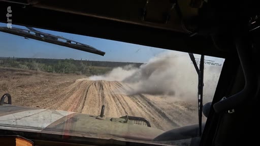 Vue subjective depuis le poste de pilotage d'un véhicule militaire en mouvement sur un terrain accidenté et poussiéreux, illustrant le quotidien des soldats en zone de conflit.