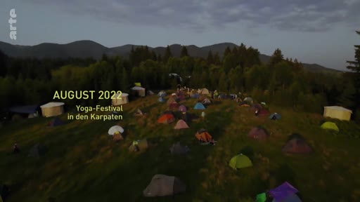 Vue aérienne d'un campement de tentes lors d'un festival de yoga dans les Carpates en août 2022. L'image montre une multitude de tentes installées dans une zone montagneuse boisée.