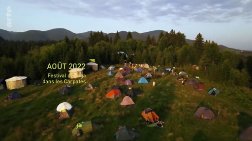 Vue aérienne d'un campement de tentes installé dans une zone montagneuse lors du festival de yoga dans les Carpates en août 2022. L'image montre une multitude de tentes dispersées sur une colline verdoyante au milieu d'une forêt.