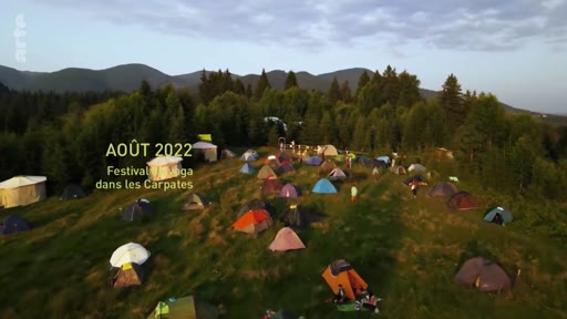 Vue aérienne d'un campement de tentes lors d'un festival de yoga organisé dans les Carpates en août 2022. Le paysage montagneux et verdoyant accueille de nombreux participants en plein air.