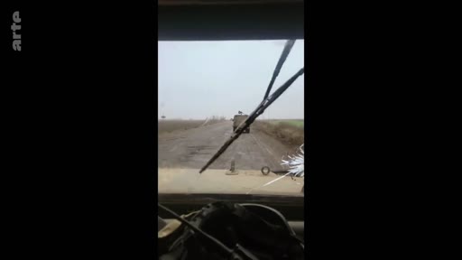 Vue subjective depuis le poste de conduite d'un véhicule militaire circulant sur une route rurale, illustrant le quotidien des soldats sur le terrain.