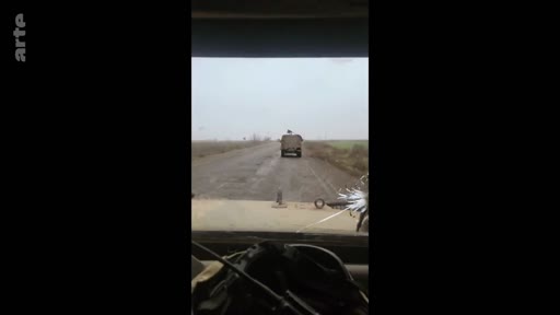 Vue subjective depuis l'intérieur d'un véhicule militaire en mouvement sur une route rurale, illustrant le quotidien des soldats sur le terrain.
