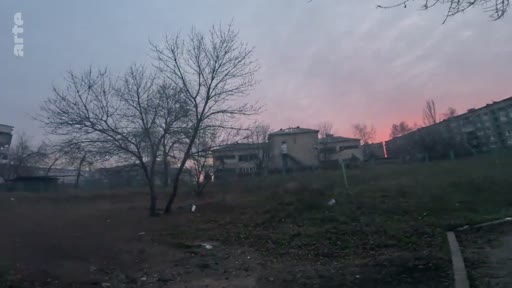Vue extérieure d'un quartier résidentiel avec des immeubles d'habitation et des arbres dénudés sous un ciel crépusculaire, illustrant le contexte urbain d'une zone potentiellement touchée par un conflit.