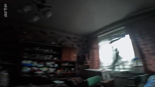 Vue intérieure d'une pièce d'habitation montrant des dégâts matériels, avec une fenêtre brisée donnant sur l'extérieur, illustrant les conditions de vie sur la ligne de front.