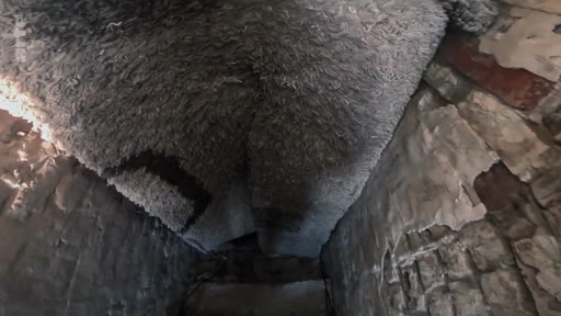 Vue en contre-plongée d'un tapis gris épais suspendu au plafond d'une cave aux murs de briques dégradés, illustrant les conditions de vie précaires d'un soldat dans un sous-sol.