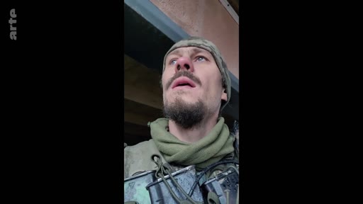 Un soldat ukrainien portant un uniforme militaire et un bonnet regarde vers le haut, illustrant la vie sous la menace constante de la guerre en Ukraine.