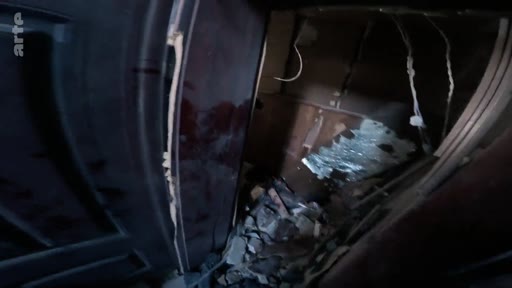 Vue intérieure montrant des débris et des dommages structurels dans un bâtiment, illustrant les conséquences d'un conflit ou d'une attaque.