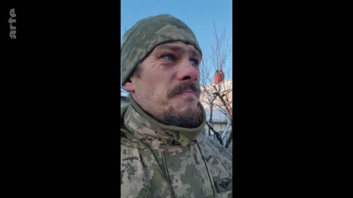 Un soldat ukrainien en tenue de camouflage et bonnet militaire témoigne lors d'une séquence vidéo, probablement depuis le front en Ukraine. Le plan serré met en avant le visage du militaire dans un contexte de conflit armé.