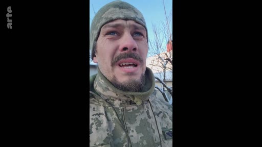 Un soldat ukrainien en tenue de camouflage et bonnet militaire s'adresse à la caméra lors d'un témoignage sur le terrain, probablement dans le cadre d'un reportage sur le conflit en Ukraine.