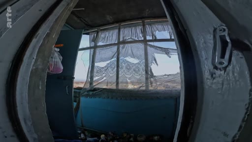 Vue intérieure d'un bâtiment abandonné ou endommagé, montrant une fenêtre avec des rideaux déchirés et des débris, évoquant un contexte de conflit ou de dévastation.