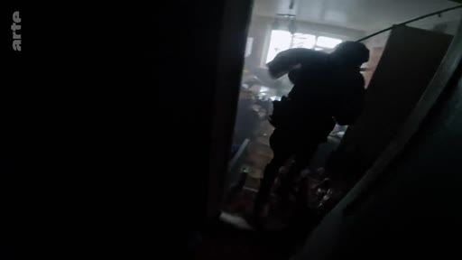 Un soldat en tenue de combat, vu en silhouette, progresse dans un couloir sombre lors d'une opération militaire. L'image illustre la tension et l'immersion au cœur d'une zone de conflit.