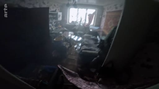 Vue intérieure d'une pièce d'habitation en désordre et endommagée, témoignant des conséquences d'une attaque ou d'un conflit. L'image montre les débris et les dégâts matériels dans un environnement domestique.