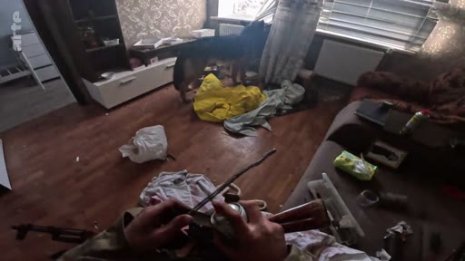 Un soldat en vue subjective manipule une arme à feu dans une pièce encombrée où se trouve un chien, illustrant le quotidien des combattants lors de l'encerclement.