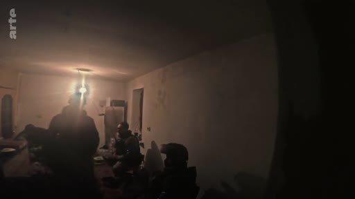 Des soldats ukrainiens équipés de matériel militaire se trouvent à l'intérieur d'un bunker faiblement éclairé, illustrant les conditions de vie sur le front en Ukraine.