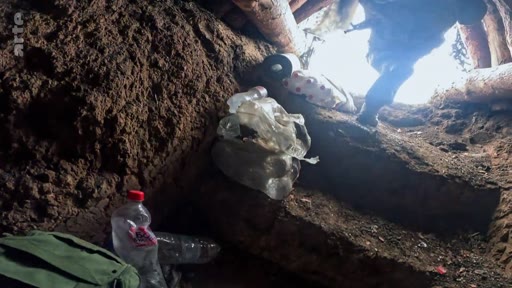Un soldat est filmé en train de sortir d'une tranchée de combat aménagée avec des rondins de bois, illustrant les conditions de vie précaires sur le front.