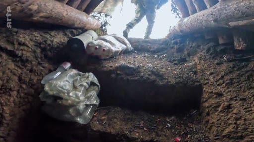 Un soldat en tenue de camouflage sort d'une tranchée militaire fortifiée avec des rondins de bois, illustrant les conditions de vie sur le front.