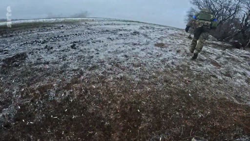 Un soldat ukrainien en tenue de camouflage court sur un terrain boueux et enneigé lors d'une opération militaire. L'image illustre la réalité du conflit en Ukraine et les conditions difficiles sur le front.