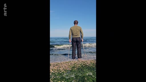 Un homme vu de dos, debout sur une plage avec des béquilles, regarde l'horizon marin. Cette image illustre la résilience et la recherche de sérénité face à la mer.