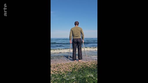 Un homme vu de dos, utilisant des béquilles pour se tenir debout, contemple l'horizon au bord de la mer. Cette image illustre la résilience et la recherche de sérénité dans la nature malgré un handicap physique.