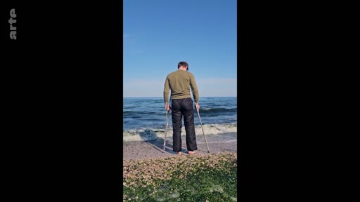 Un homme debout de dos sur le rivage, utilisant des béquilles pour se tenir face à l'océan, illustrant la résilience et la rééducation physique en extérieur.