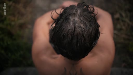 Vue en plongée sur le dos d'un homme montrant un tatouage, illustrant le traumatisme et les cicatrices psychologiques liées à la guerre.