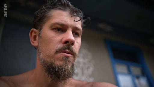 Un homme barbu, filmé en gros plan, semble plongé dans une réflexion profonde, illustrant le thème de la quête de libération personnelle.