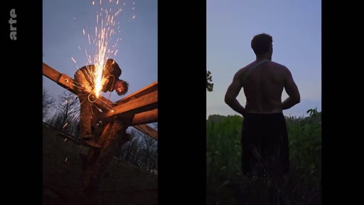 Un ouvrier utilise une meuleuse pour travailler sur la structure métallique du centre Goloka, tandis qu'un homme torse nu observe le paysage environnant au crépuscule. Cette scène illustre les travaux de construction du centre Goloka.