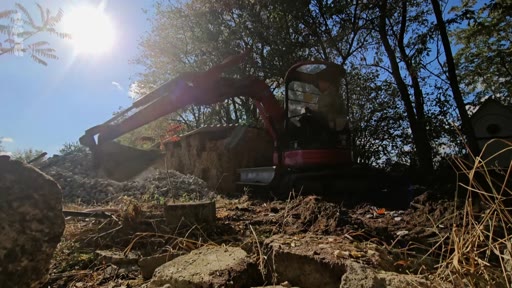 Une mini-pelle de chantier déblaie des gravats sur le site de construction du centre Goloka, illustrant les travaux de terrassement en cours.