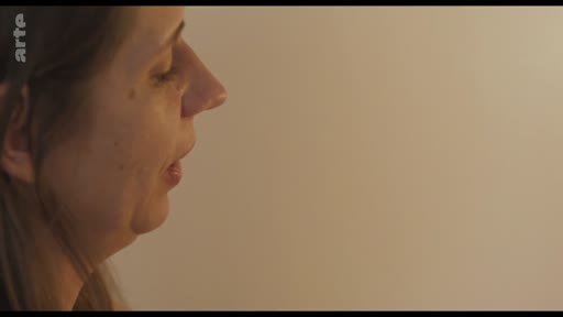 Gros plan sur le visage d'une femme s'exprimant de profil, dans une séquence illustrant le thème de la visite inattendue.