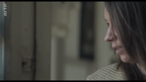 Une femme, vue de profil, observe l'extérieur à travers une fenêtre dans une atmosphère calme et silencieuse. L'image capture un moment d'introspection ou d'attente.