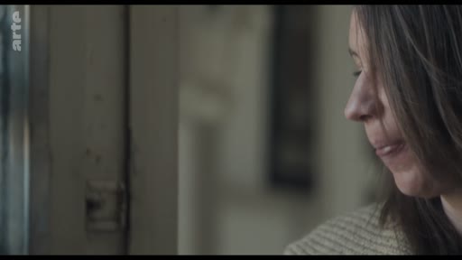 Une femme est filmée en gros plan de profil alors qu'elle regarde par une fenêtre, dans une atmosphère calme et silencieuse.