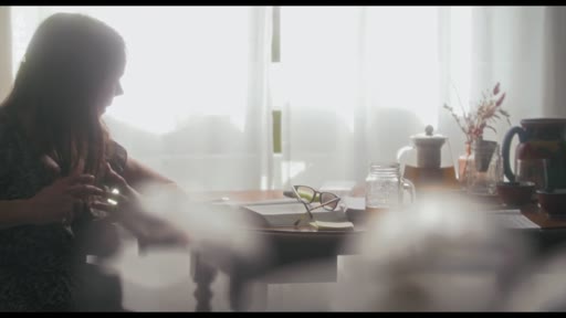 Une femme est assise à une table près d'une fenêtre lumineuse, en train de lire un livre. L'ambiance est calme et studieuse, typique d'une scène de préparation ou de réflexion dans le cadre d'une interview sur la création de personnages.